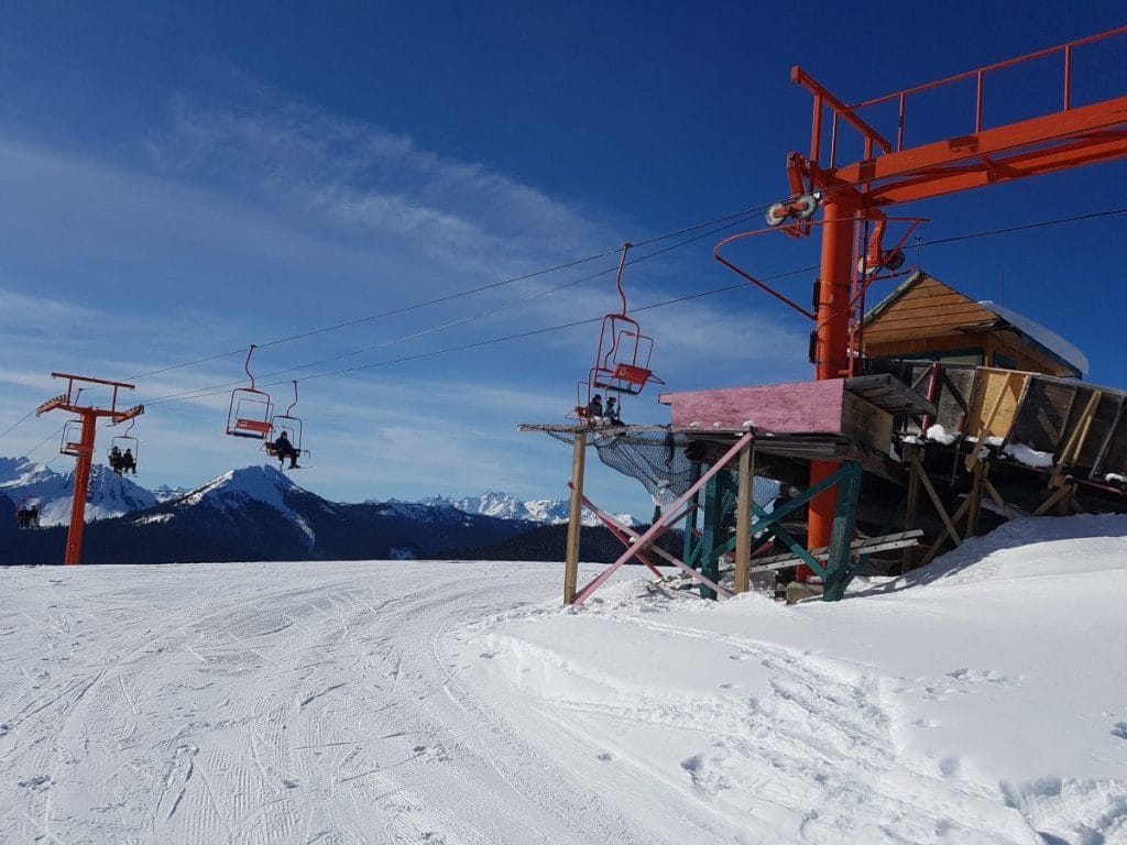 A ski lift with red chairs and support poles operates on a snowy mountain slope at one of the premier ski resorts in the Fraser Valley, with snow-covered peaks visible in the background under a clear blue sky.