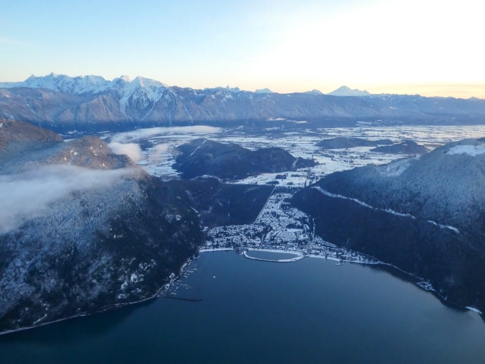 Aerial view of a snowy town beside a lake, surrounded by mountains under a clear sky at sunrise—perfect for enjoying winter activities in Harrison Hot Springs.