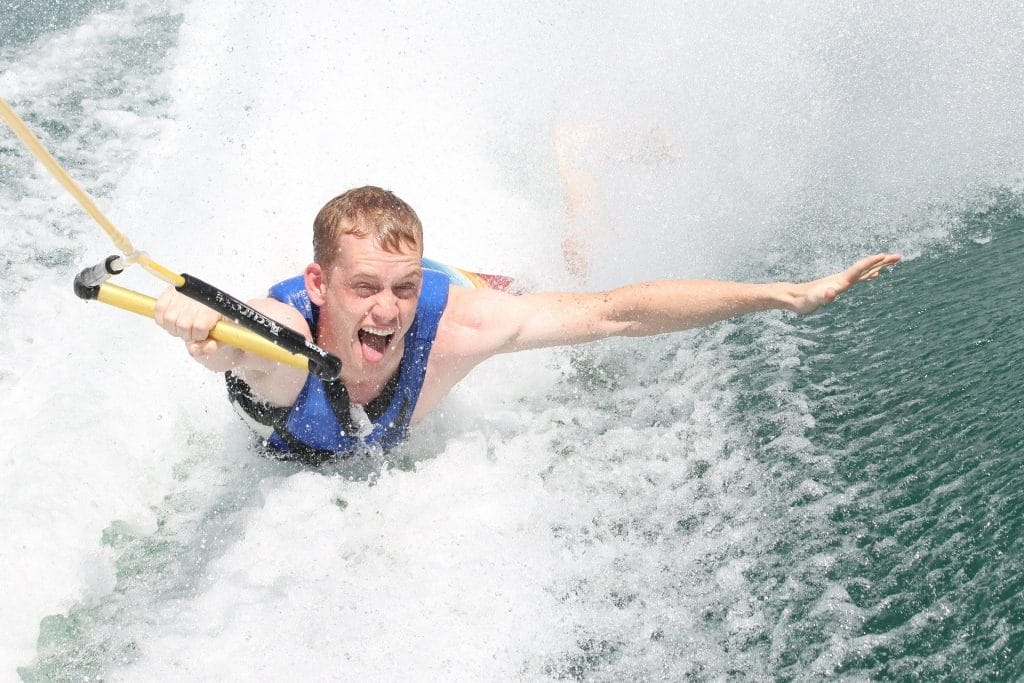 A person wearing a blue life jacket water skiing at Cultus Lake, holding onto a tow rope with one hand and extending the other arm, with water splashing behind them—one of the thrilling things to do in Cultus Lake.