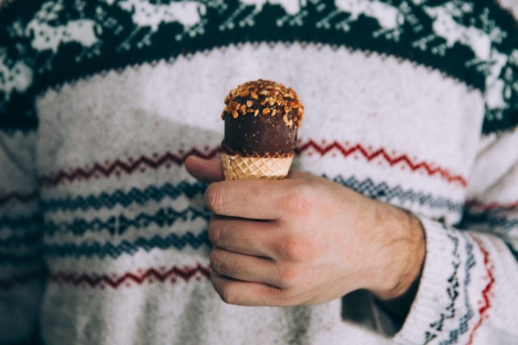 A person wearing a patterned sweater enjoys an ice cream cone topped with chocolate and nuts—one of the delightful things to do in Cultus Lake.