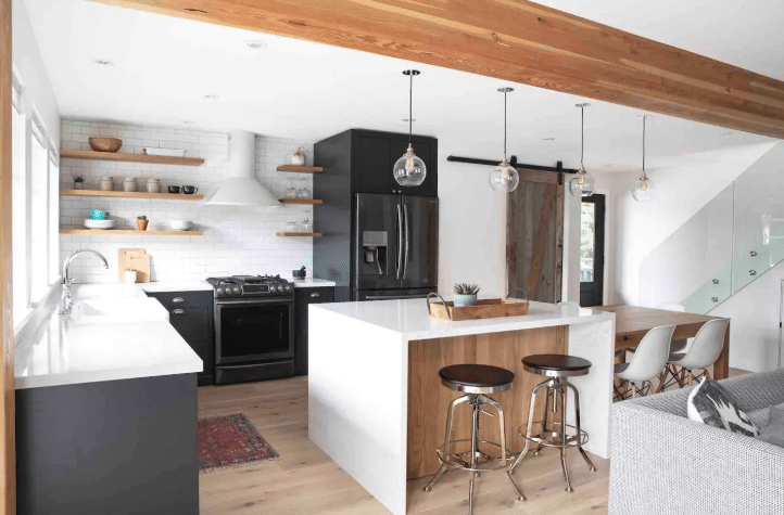 Modern kitchen with white countertops, black appliances, a central island with two stools—perfect to set up an Airbnb listing—plus open shelves and a dining area featuring a wooden table and white chairs.
