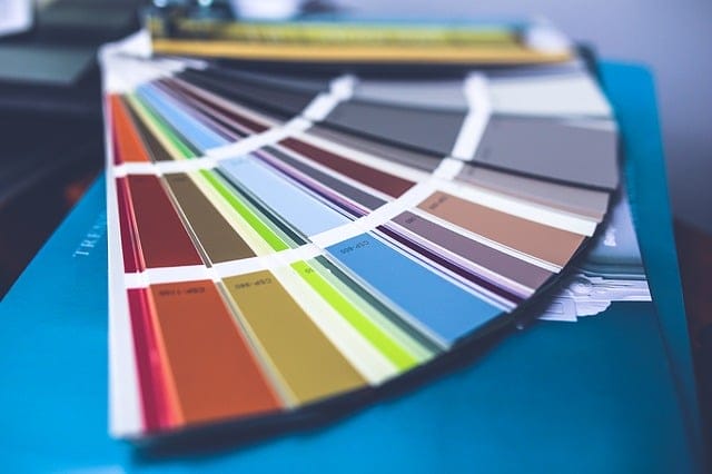 A close-up of a fanned-out color swatch book displaying various paint color samples on a blue surface—perfect inspiration for your next do it yourself Airbnb makeover.