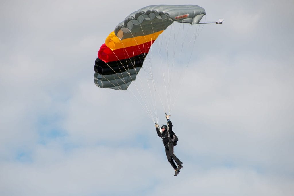 A person in black clothing is parachuting with a gray, red, yellow, and black parachute against a cloudy sky—one of the thrilling things to do in Harrison Hot Springs.