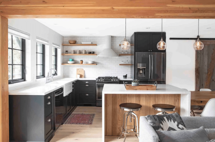 Modern kitchen perfect for a New Airbnb Guest, featuring black cabinets, white countertops, open wooden shelves, stainless steel appliances, and three pendant lights above a wooden island with two stools.