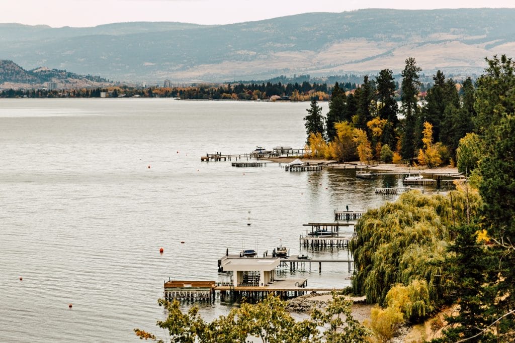 Lakeside view with boat docks along the shore, trees with autumn foliage, and mountains in the background under an overcast sky—one of the best places to visit in BC for stunning natural scenery.