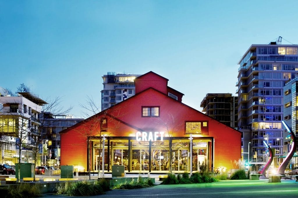 A large red building labeled "CRAFT" stands illuminated at dusk, surrounded by modern apartment buildings and city lights, capturing the vibrant atmosphere of Airbnb Property Management Vancouver.