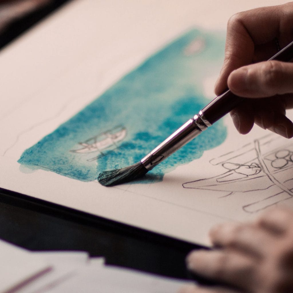 A hand uses a paintbrush to apply blue watercolor paint to a sketch of a scene on white paper—one of the creative things to do in Ucluelet for art lovers and visitors alike.