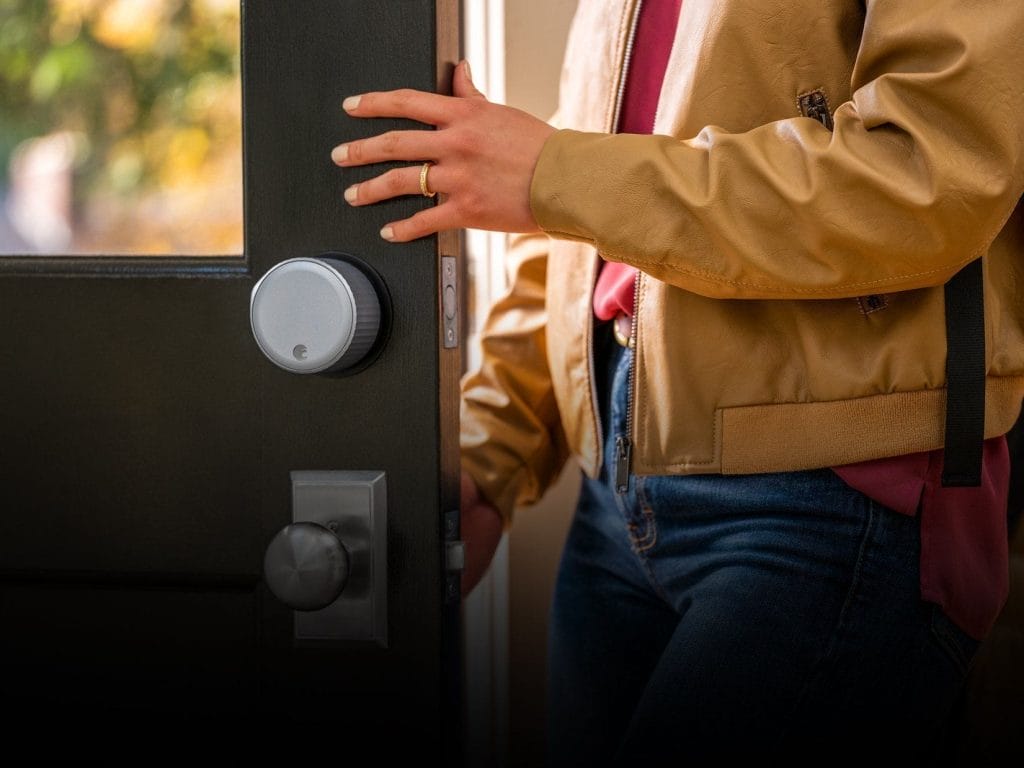 A person wearing a tan jacket opens a door equipped with an Airbnb smart home lock and standard door knob.