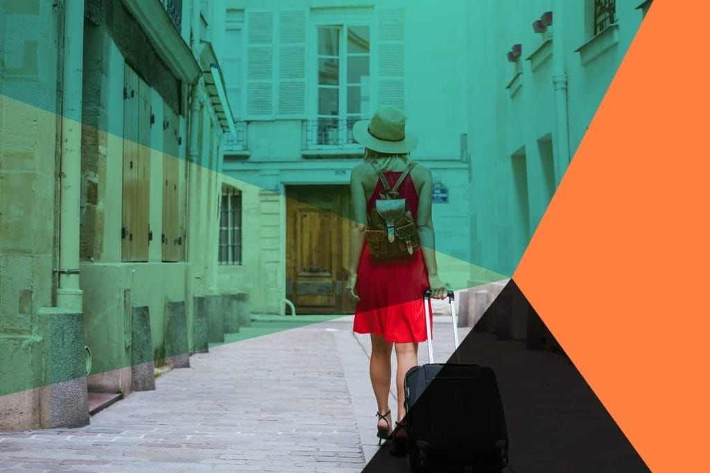 A person in a red dress and hat walks down a narrow street with a suitcase, overlaid with geometric colored shapes, evoking the sense of adventure that Vacation Rental Software brings to travel planning.
