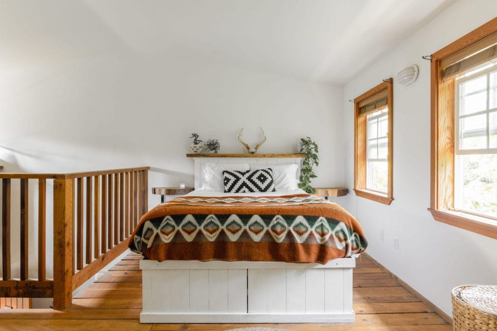 A neatly made bed with geometric-patterned bedding sits in a bright room with wood floors, white walls, and two windows letting in natural light—perfect for testing the best Airbnb cameras for crisp room photography.