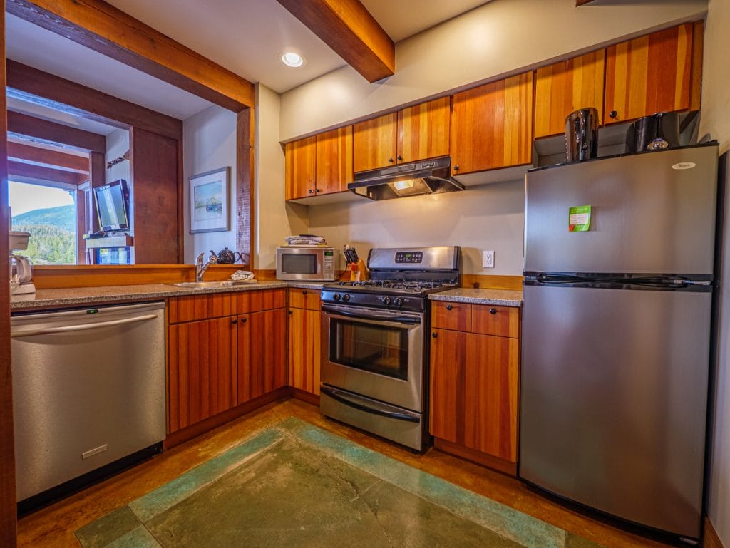 Modern kitchen with wood cabinets and stainless steel appliances—stove, refrigerator, dishwasher, and microwave—under bright recessed lighting, perfect for a stylish Vacation Rental Design.