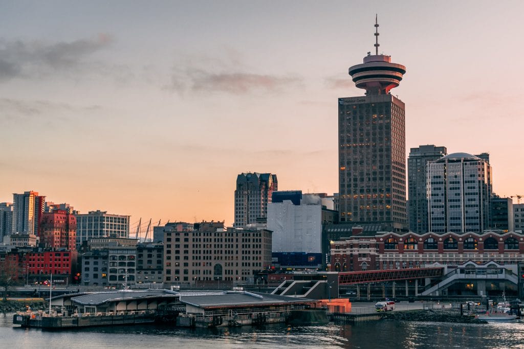 Downtown cityscape at sunset featuring high-rise buildings and a distinctive tower, with waterfront structures in the foreground—an inspiring view that highlights the growth of remote work in BC.