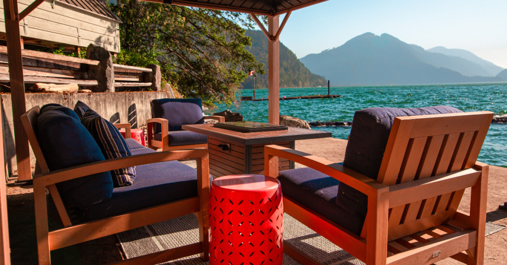 Outdoor seating area with wooden chairs and blue cushions under a gazebo, overlooking a lake and mountains—a perfect inspiration for how to setup an Airbnb that wows guests on a sunny day.