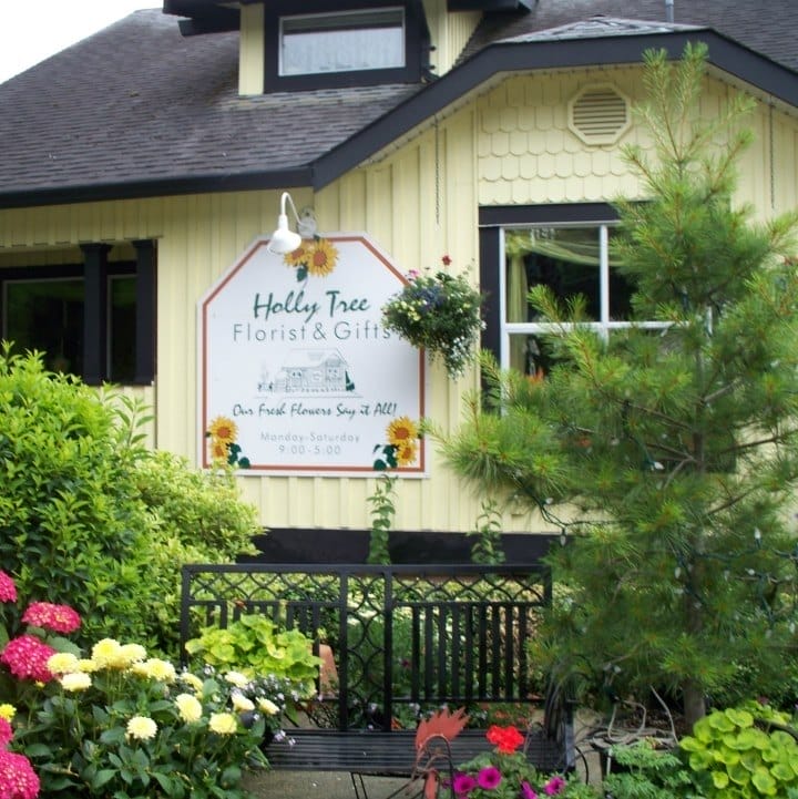 A flower shop called "Holly Tree Florist & Gifts" is surrounded by blooming flowers, plants, and greenery in front of a cream and brown building—perfect for your Harrison Hot Springs wedding floral needs.