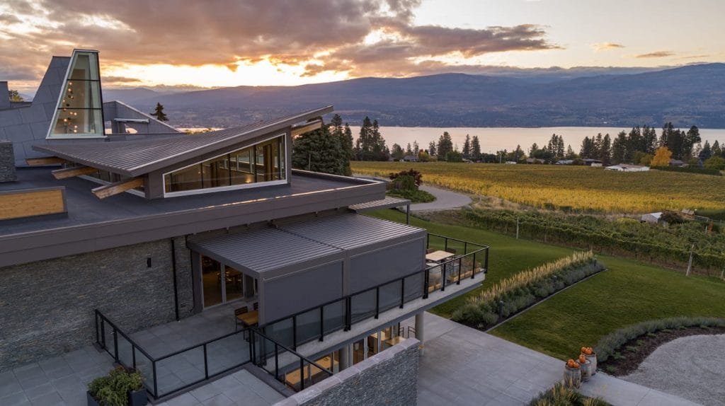 Modern house with angular roof and large terrace overlooking a vineyard, lake, and mountains at sunset—perfectly situated near the best West Kelowna wineries. Manicured lawn and landscaped garden complete the stunning foreground.