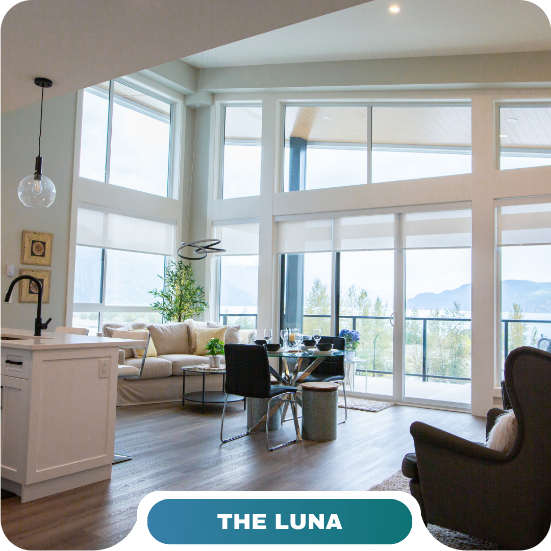 Modern living room with large windows, a kitchen island, dining table, and seating area. Bright natural light fills the space—perfect for vacation rentals in Harrison Hot Springs. Text at the bottom reads "THE LUNA.