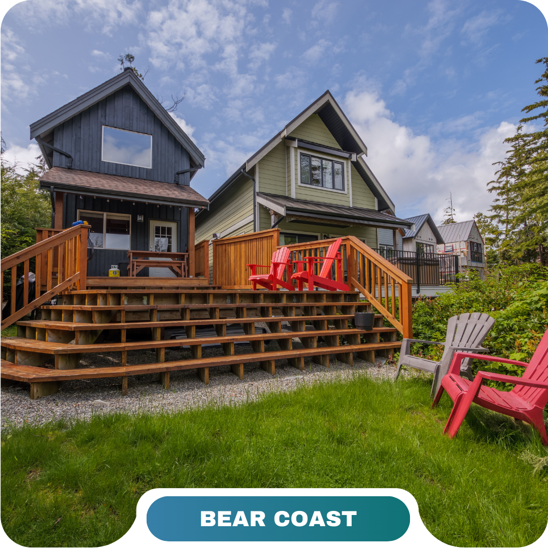 Two houses with wooden decks and red and gray Adirondack chairs on a grassy lawn under a partly cloudy sky; labeled "Bear Coast," perfect for relaxing vacation rentals in Big White.