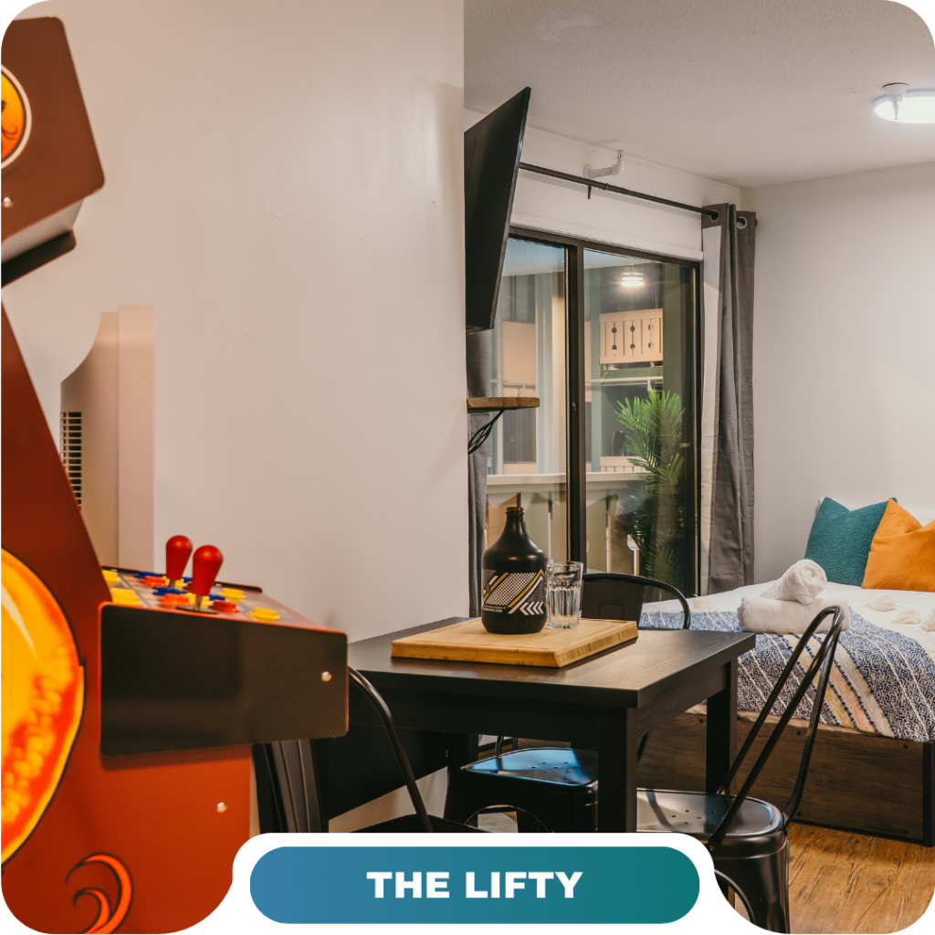 A modern studio featuring a bed, dining table, wall-mounted TV, large window, and an arcade game machine—the perfect option for vacation rentals in Big White.