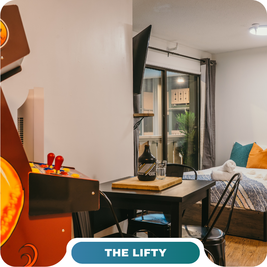 A modern studio featuring a bed, dining table, wall-mounted TV, large window, and an arcade game machine—the perfect option for vacation rentals in Big White.