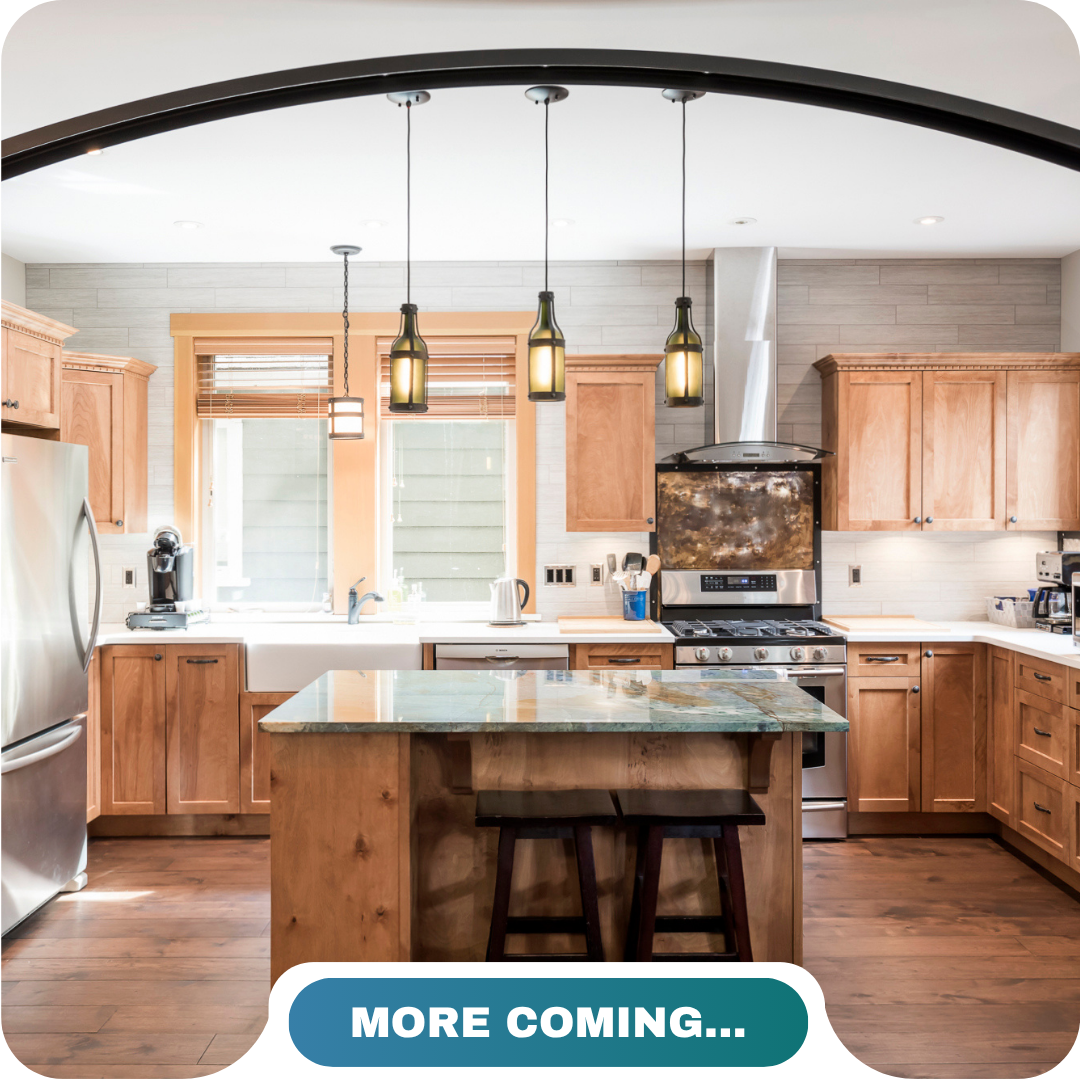 Modern kitchen with wooden cabinets, stainless steel appliances, an island with two stools, and pendant lights; perfect for vacation rentals in Cultus Lake. Text at bottom reads "MORE COMING…".