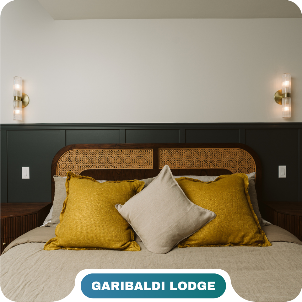 A neatly made bed with yellow and beige pillows, dark wood headboard, and wall-mounted lights in a room labeled "Garibaldi Lodge," showcasing the comfort found in vacation rentals in Whistler.