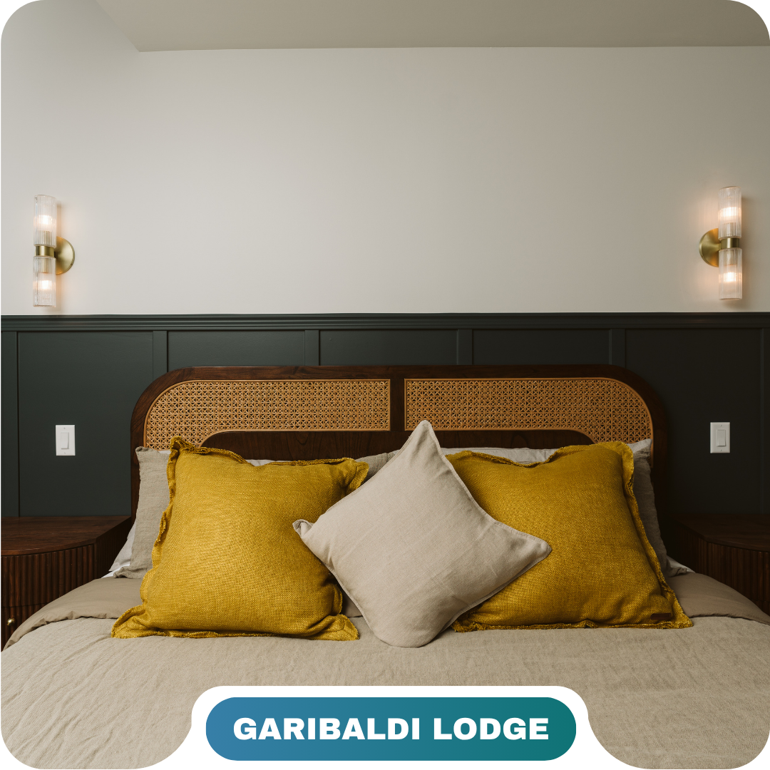 A neatly made bed with yellow and beige pillows, dark wood headboard, and wall-mounted lights in a room labeled "Garibaldi Lodge," showcasing the comfort found in vacation rentals in Whistler.
