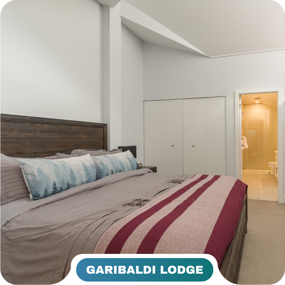 A neatly made bed with tree-themed pillows and a red-striped blanket sits in a bedroom with white walls, a closet, and an ensuite bathroom—perfect for those seeking vacation rentals in Whistler. Text reads "GARIBALDI LODGE.