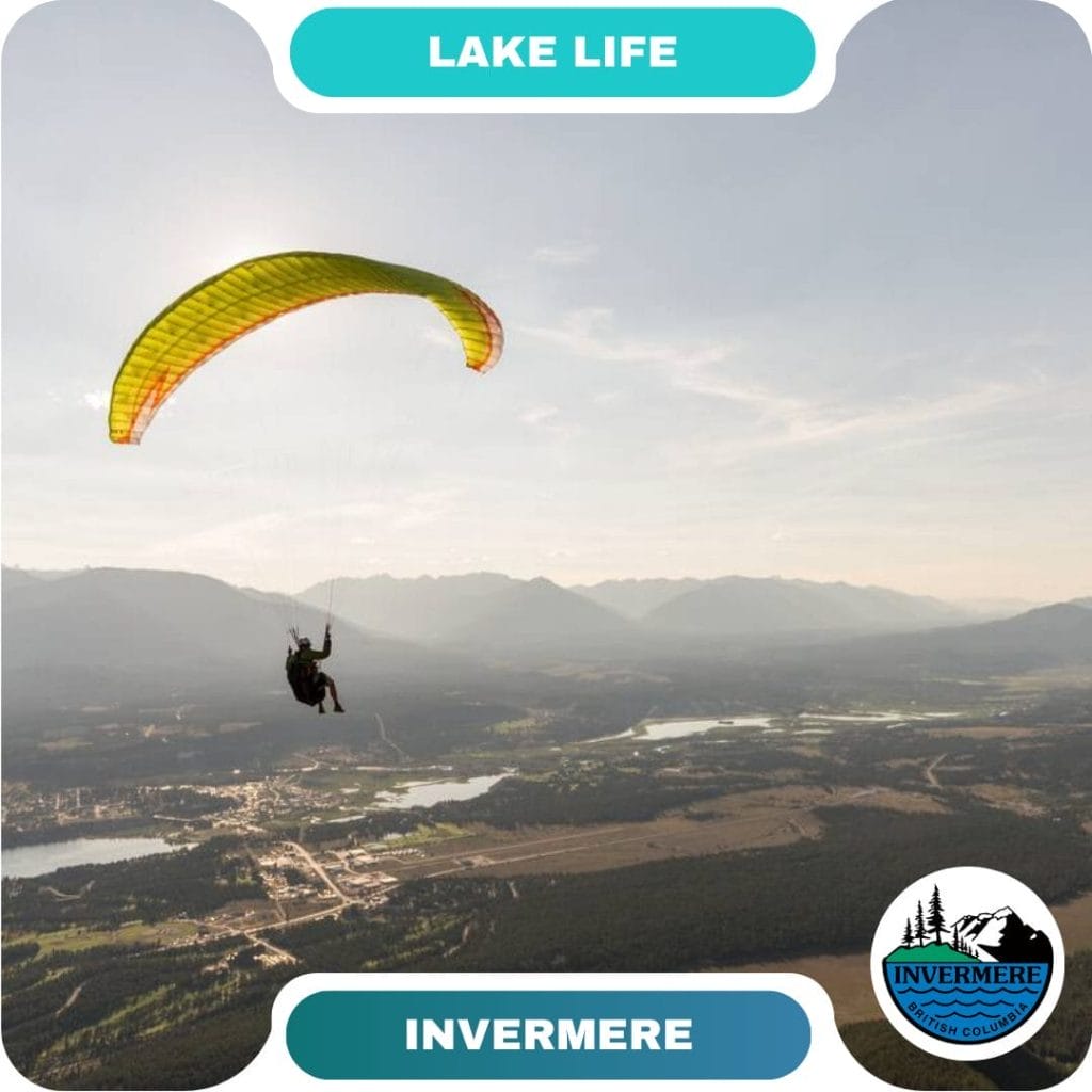 A guest paraglides high above a valley of lakes, forests, and mountains; text reads "Lake Life" and "Invermere" with a logo in the bottom right corner, highlighting one of the region's top destinations.