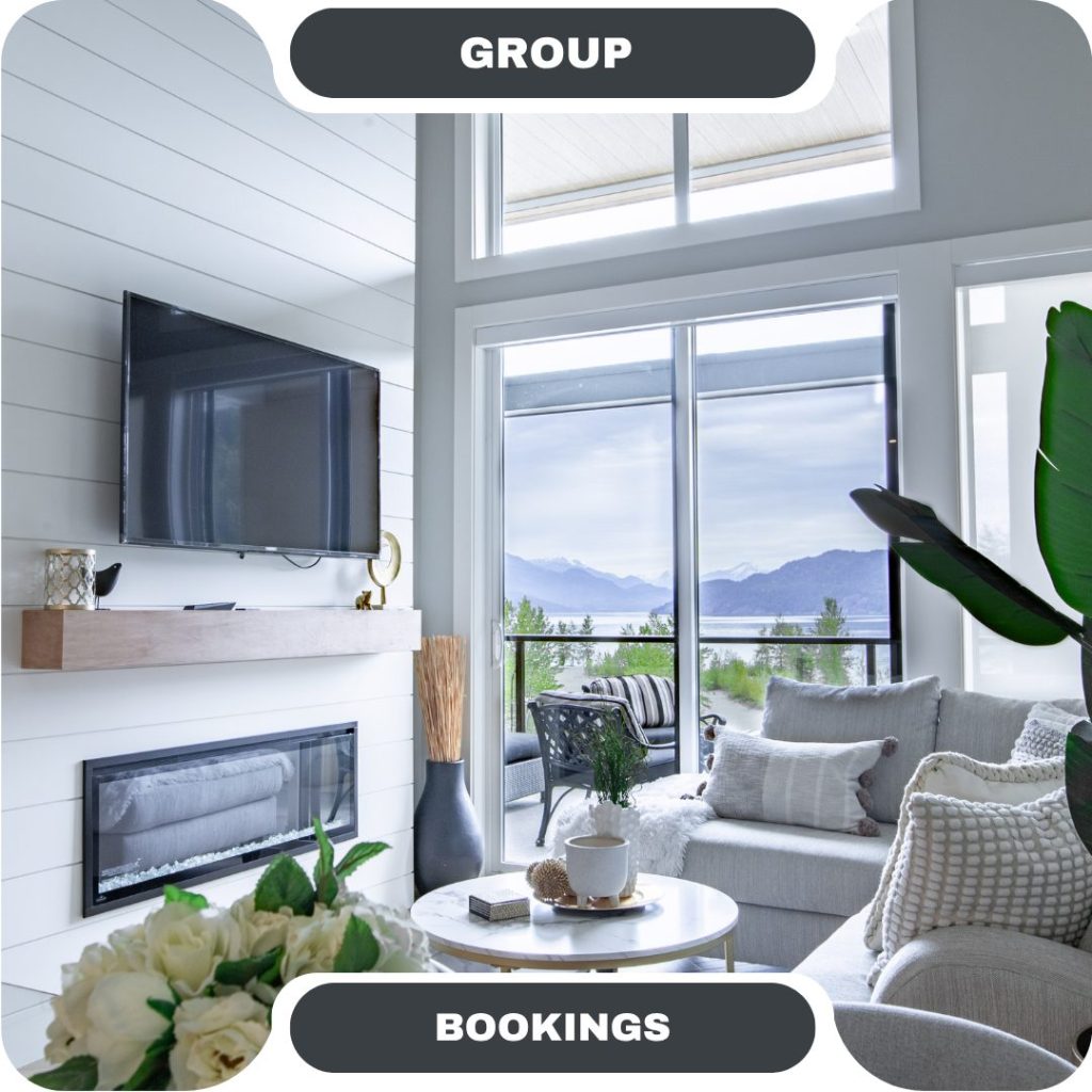 Modern living room in furnished rentals with a wall-mounted TV, fireplace, large windows offering mountain views, a sectional sofa, and contemporary decor.