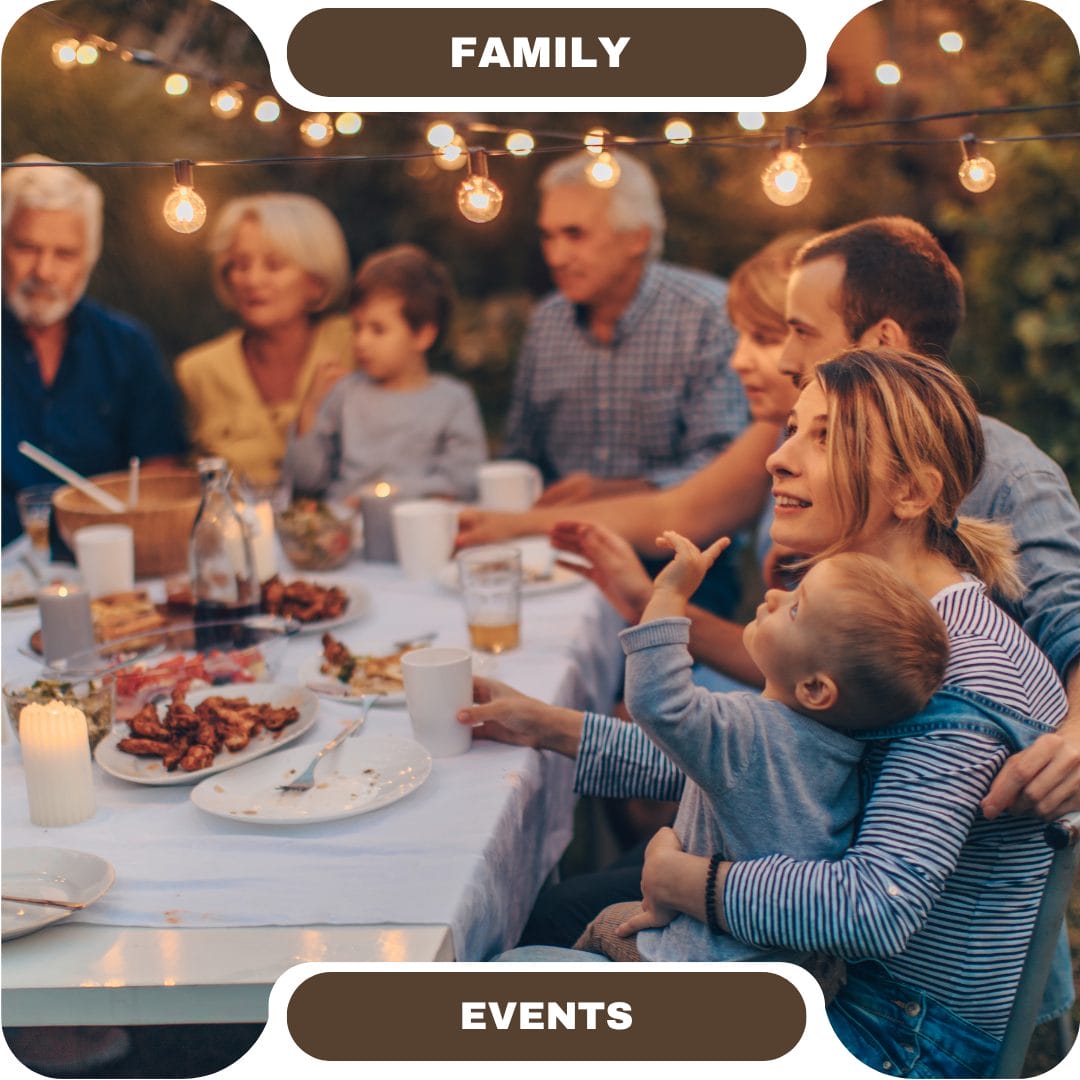 A family group sits around a table outdoors, sharing a meal under string lights during a gathering at one of the cozy furnished rentals.
