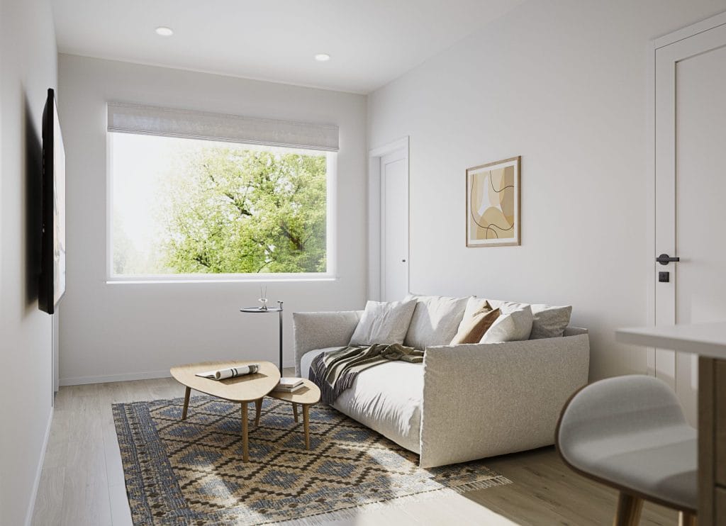 Modern living room at Cultus Grove with a large window, light-colored walls, a gray sofa, wooden coffee table, geometric rug, and wall art; sunlight fills the space.