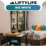 A cozy studio room with a bed, colorful pillows, small dining table, chairs, and an arcade machine; perfect for those interested in buying property or exploring real estate at Big White. A window and door sit beneath a “Liftylife Big White” banner.