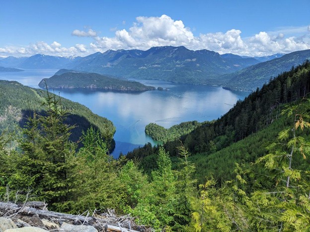 A scenic view of a blue lake surrounded by forested hills and mountains under a partly cloudy sky, perfect for exploring Harrison Hot Springs attractions and discovering new things to do in Harrison Hot Springs.