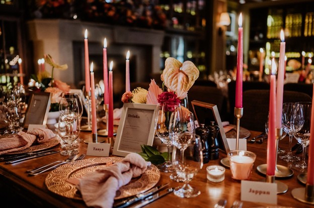 A decorated dinner table set with pink candles, glassware, name cards, menus, and floral centerpieces in a warmly lit indoor setting—perfect inspiration for planning a wedding in Whistler.