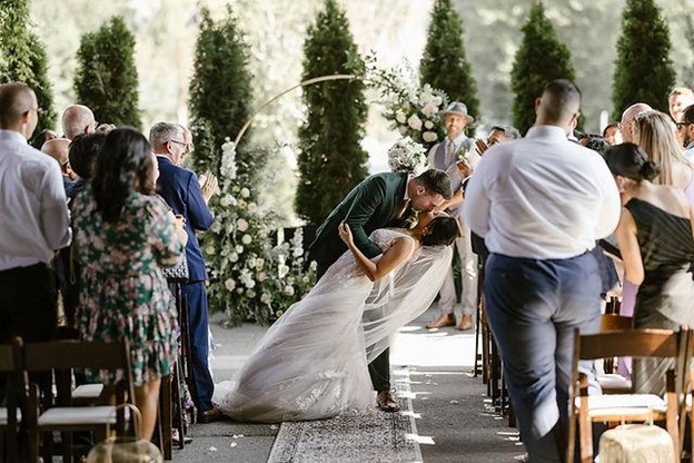 A bride and groom share a kiss at the end of the aisle during an outdoor wedding ceremony in Whistler as guests stand and applaud—perfect inspiration for anyone planning a wedding in Whistler.